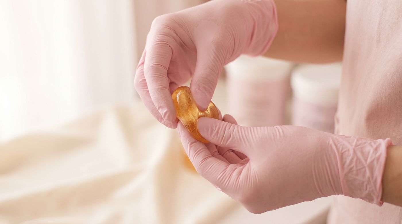 Gloved hands working a ball of golden sugar paste